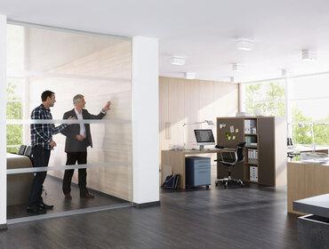 Impression eines Büros mit abgeschlossenem Raum mit Glaswand und offener Bürogestaltung.